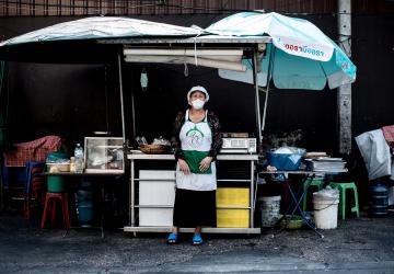Sawan Panthaisong, une vendeuse de produits alimentaires se tient debout devant son stand de nourriture, face à la caméra, à Sukhumvit Soi 20, à Bangkok, en Thaïlande.