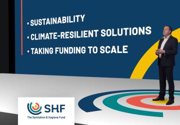 Dominic O'Neill presenta el nuevo Fondo de Saneamiento e Higiene mientras se para frente a una pantalla grande que muestra una presentación.