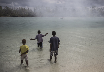 Tres pequeños se encuentran en una masa de agua mientras observan un barco cercano. 