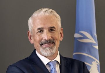 A man with his arms crossed stands in front of the United Nations flag.