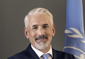 A man with his arms crossed stands in front of the United Nations flag.