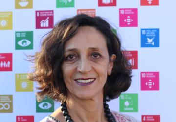 A smiling woman stands in front of a poster of the United Nations Sustainable goals.