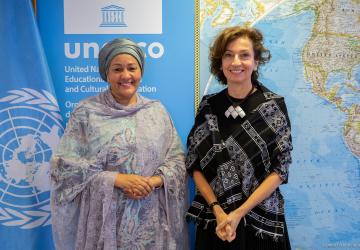 Two women - high-ranking UN officials - pose for a picture in front of a map and a UN flag.