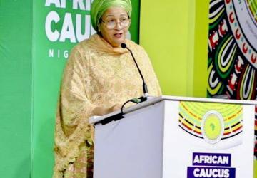 The DSG standing by the podium in front of a green backdrop. The podium has the African Caucus branding