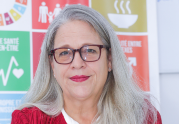 A woman in a red suit blazer against a backdrop of the SDGs.
