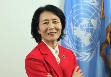 A woman in a red suit blazer against a blue UN flag