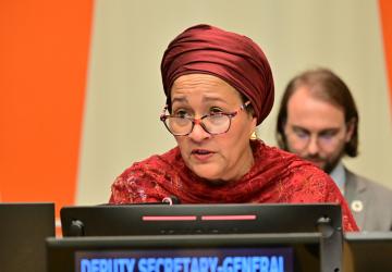 A woman in brown dress and headscarf, the DSG of the United Nations, speaks into a microphone in a podium.