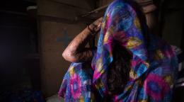 Une femme est assise par terre. Elle regarde la caméra, mais sa robe recouvre entièrement sa tête et son visage.