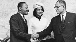 Black and white photo of Dr. Martin Luther King and his wife Coretta Scott King are seen being greeted by Mr. Ralph J. Bunche, UN Under-Secretary for Special Political Affairs in 1964.