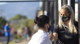 Una maestra revisa la temperatura de una niña antes de entrar a la escuela por la puerta.