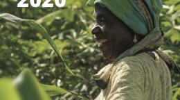 Une femme se tient au milieu d'un champ agricole verdoyant en arborant un grand sourire.