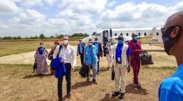 ينزل أشخاص عدة يرتدون أقنعة الوجه ويحملون أكياسًا وسترات إلى حقل في يوم مشمس.