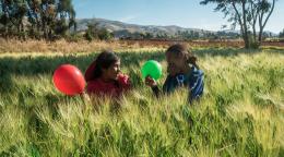Deux petites filles jouent en riant avec un ballon vert et un ballon rouge dans un champ.