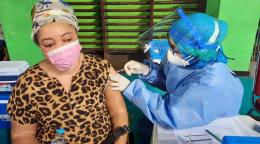 A healthcare professional gives a refugee woman, wearing a mask, her first jab of the COVID-19 vaccine.