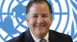 A smiling man looks straight at the camera with the United Nations Logo in the background.