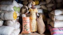 Une femme vêtue d’une robe traditionnelle africaine se tient debout dans un entrepôt à côté de nombreux sacs de semences.