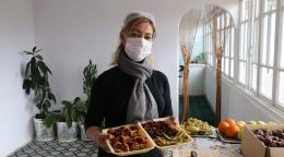 A woman wearing a white facemask showcases a takeaway food container full of dried fruits.