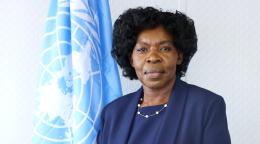 امرأة ترتدي حلة زرقاء داكنة تقف أمام علم الأمم المتحدة.