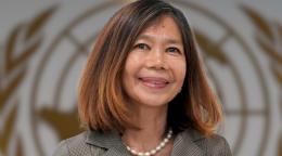 امرأة ترتدي اللؤلؤ وقميصًا تقف أمام شعار الأمم المتحدة.