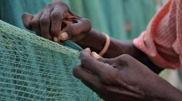 Foto en primer plano de las manos de una persona tejiendo una red de pescador.