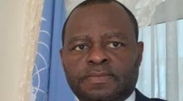 رجل يقف بجانب علم الأمم المتحدة الأزرق وينظر للكاميرا.