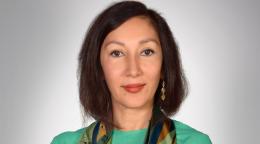 一位身穿绿色毛衣、戴着彩色围巾的妇女对着镜头微笑。