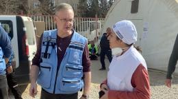 A man in a blue UN vest speaks to a rescue worker, in a white cap, amid devastation from an earthquake.