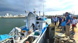 A group of people in blue vests and hats gather around a boat that sits on the water in Manabi, Ecuador