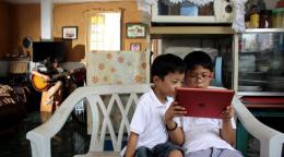 Two children in the Philippines wearing white dresses are crouched over a digital tablet screen