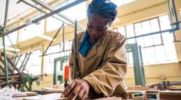 A woman in a brown shirt does woodwork on a table in a well-lit workshop