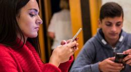 Young people look down and play on their phones.