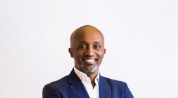 A man in a blue suit and white shirt with his arms crossed, against a white background
