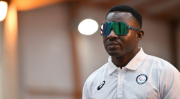 A man in a white shirt and dark visor glasses stands in a well-lit room