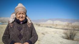 A woman in a thick jacket and a woollen cap stands amid a deserted land