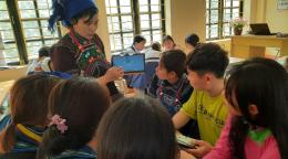 A teacher holds a tablet in front of her students in a classroom.