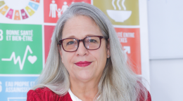 A woman in a red suit blazer against a backdrop of the SDGs.