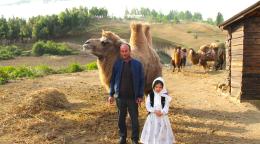 A man with his daughter with a camel in the background