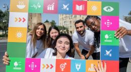 A group of volunteers, young men and women, hold up a square frame with the SDGs on it.