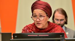A woman in brown dress and headscarf, the DSG of the United Nations, speaks into a microphone in a podium.