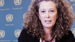 A woman in a black shirt against a blue background with UN logos