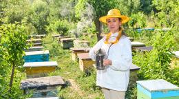An Uzbek woman beekeeper stands in front of her beekeeping operation.