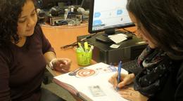 Dos mujeres trabajando juntas, sentadas frente a un escritorio donde hay una computadora.