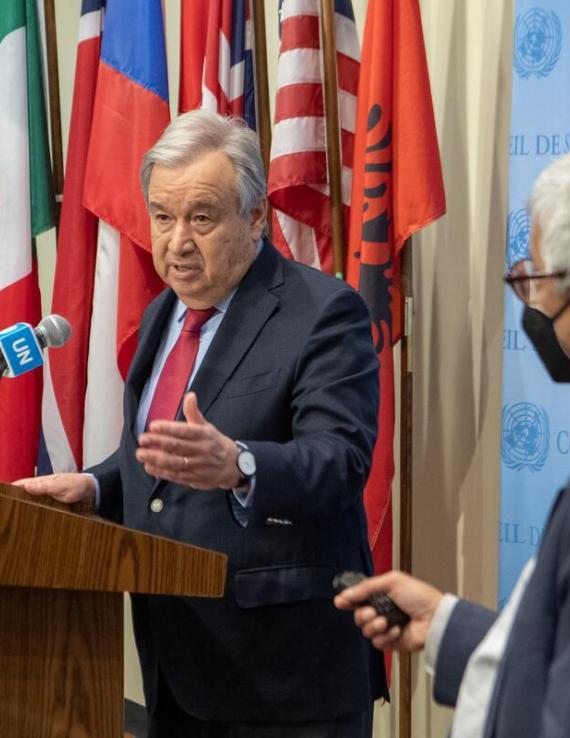 A man speaks into a microphone with flags behind him. He is the Secretary-General of the UN, briefing reporters.