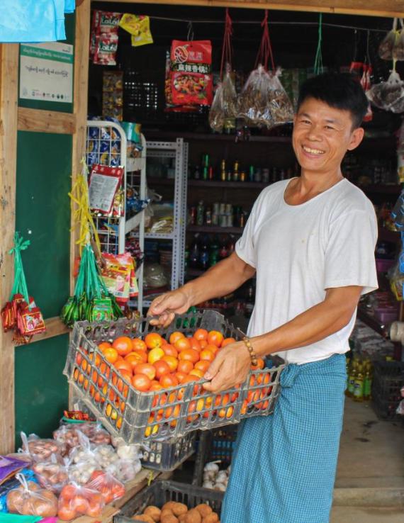 A man holds a basket of oranges, in a market place. 