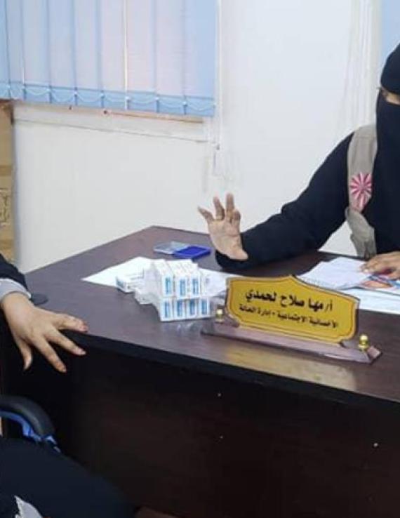 Сотрудница ЮНФПА сидит за столом и объясняет посетительнице о вреде калечащих операций