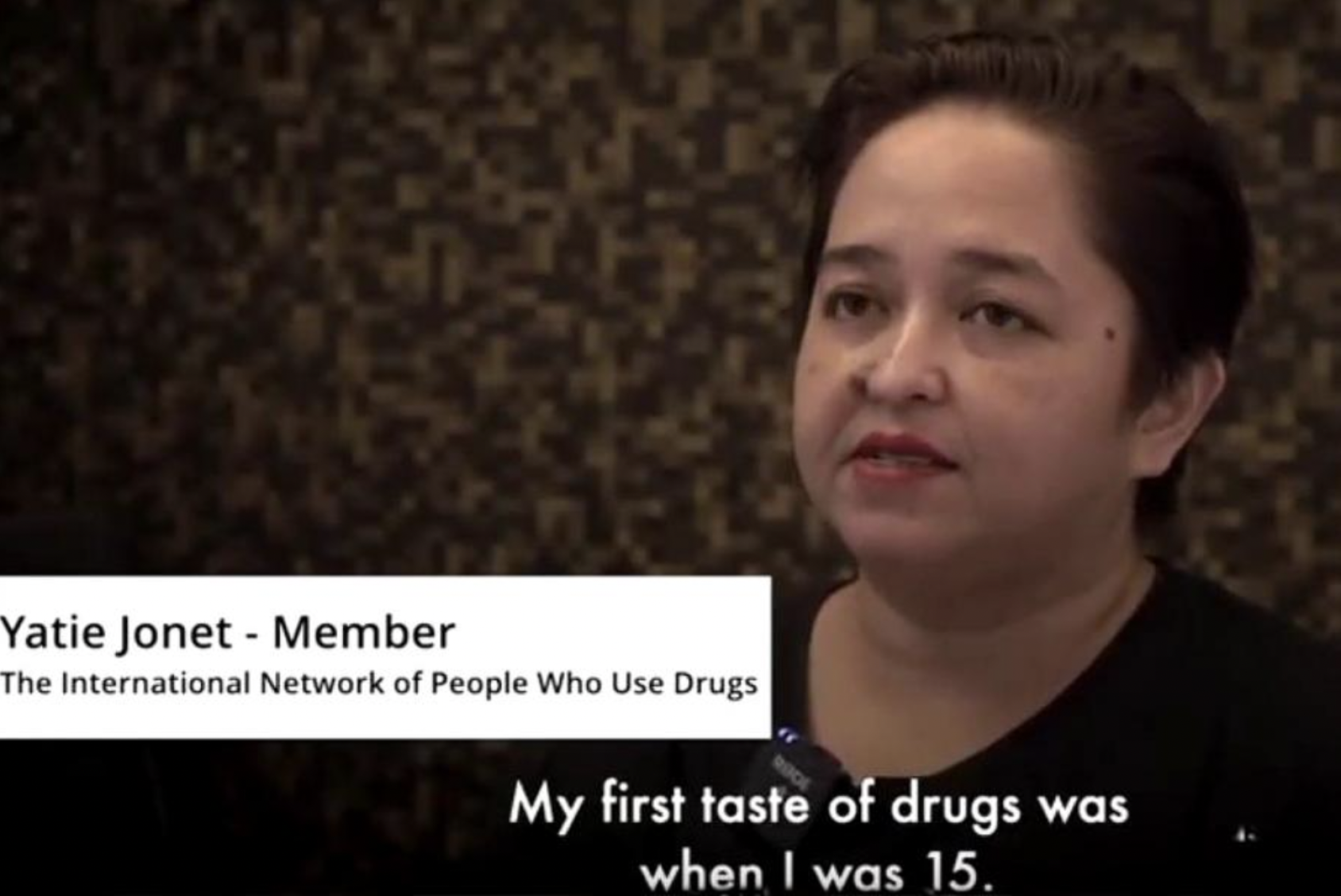 A screenshot from a video of a woman in a black shirt looking at an interviewer who is off camera. 