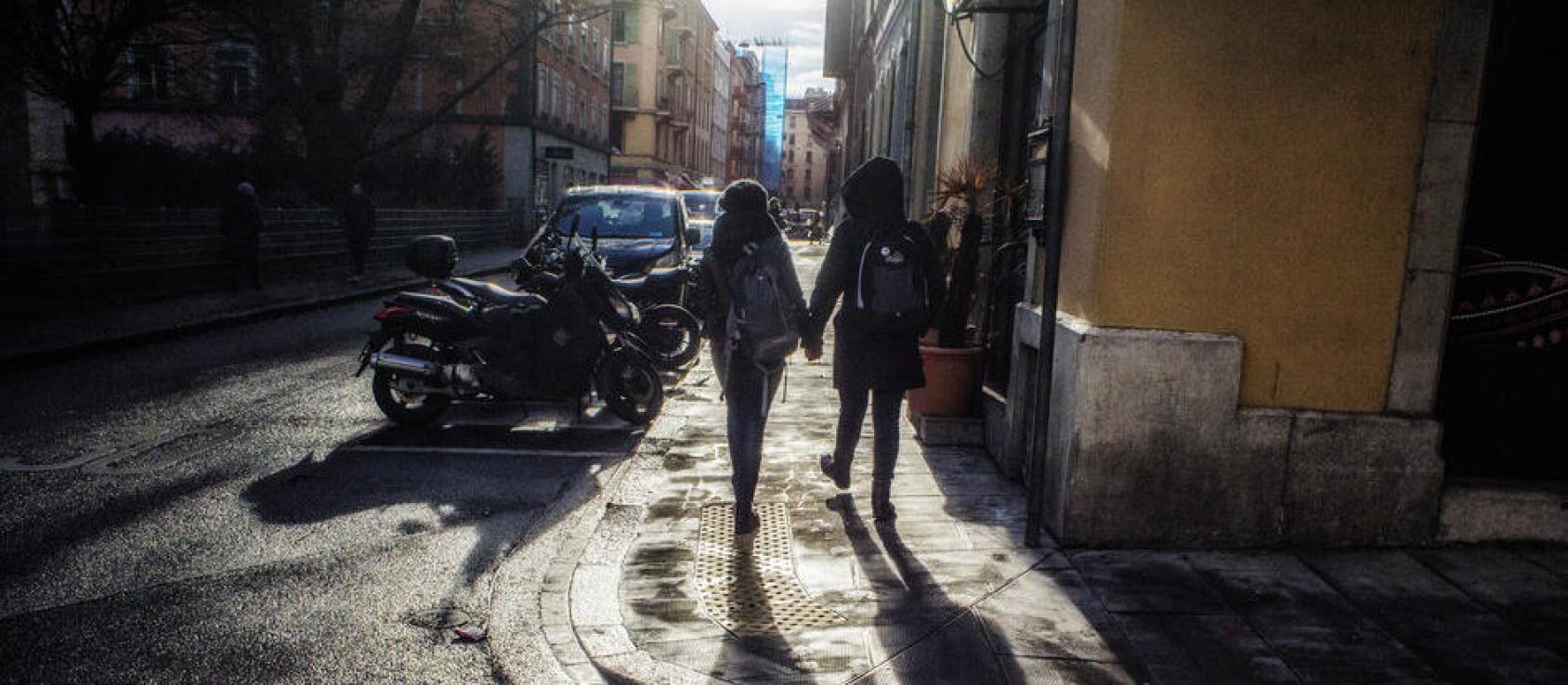 The back of two people walking down a sidewalk holding hands.