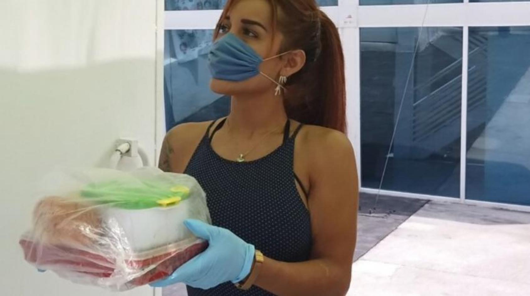 A trans woman in a face mask holds a couple of food containers in a plastic bag.