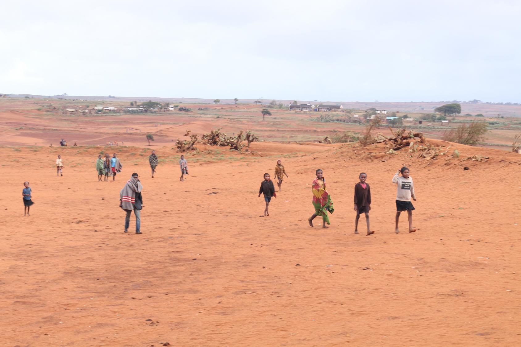 يسير العديد من الناس فوق أراضٍ زراعية مغطاة بالرمال.