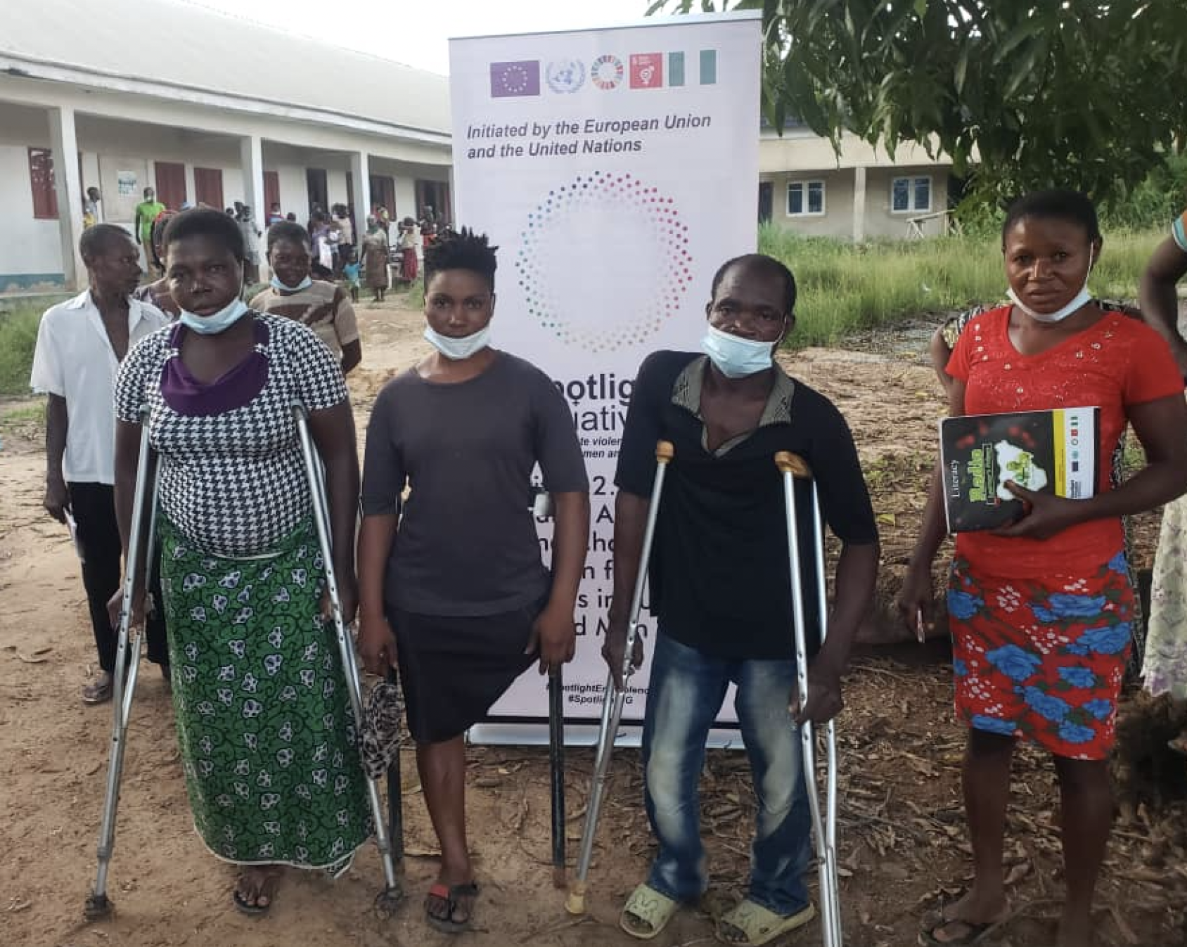 Four students stand outside a building near a white banner for the Spotlight Initiative.